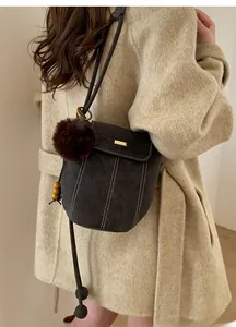 Detail of dark grey bucket bag with contrast stitching and fur pompom on wool coat