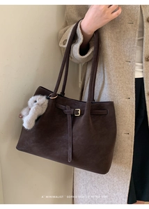 Detail of dark brown matte tote bag featuring gold buckle and soft plush bunny keychain