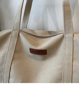 Close-up of beige canvas tote bag showing coarse texture and brown leather logo detail