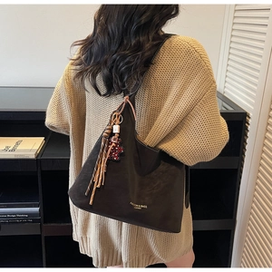 Detail of dark brown matte tote bag featuring leopard bear charm and leather tassels