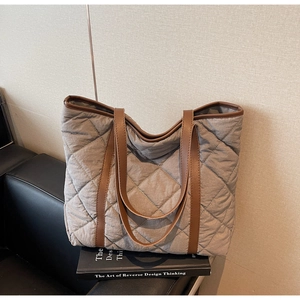Detail view of grey quilted tote bag featuring brown faux leather straps and fine stitching