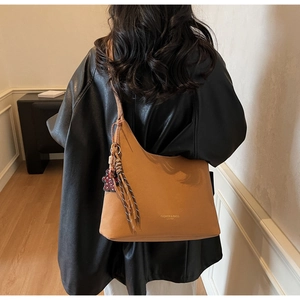 Brown leather tote bag with tassel charm shown on model's shoulder for size reference