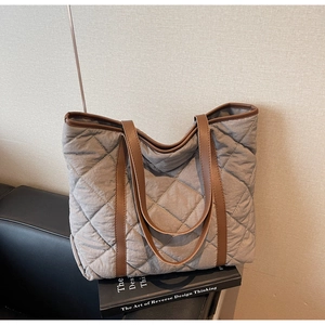 Detail of gray quilted tote bag with brown straps placed on a leather sofa for casual use