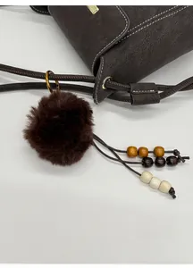 Detail of dark brown plush pompom and wooden bead tassel on a crossbody bag