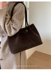 Detail of dark brown matte tote bag with thin strap and gold buckle on beige wool coat