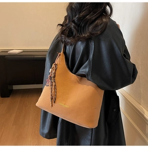 Detail of a brown leather bucket bag with fashion lettering and cute pendant on a shoulder