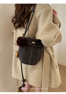 Detail of retro bucket bag with decorative stitching and fur pom-pom on beige coat