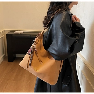 Detail of camel hobo bag featuring woven ethnic tassel and embossed fashion text
