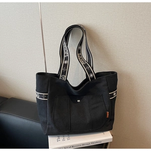Macro detail of black canvas tote bag showing embroidered SJCHAO straps and front pocket