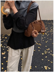 Detail of brown suede Boston bag with donut charm on autumn ginkgo leaf road