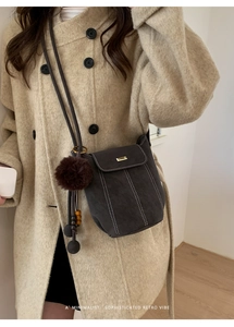 Close-up of retro charcoal bucket bag with white stitching and plush charm on beige coat