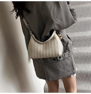 Detail of beige woven hobo bag featuring stylish wooden bead charm and leather strap