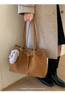 Close-up of brown leather tote bag with decorative buckle and plush rabbit charm
