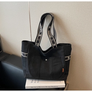 Close-up of black canvas tote bag featuring patterned ribbon handles and orange label detail