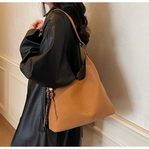 Close-up of caramel leather tote bag with gold lettering shown on a model's shoulder