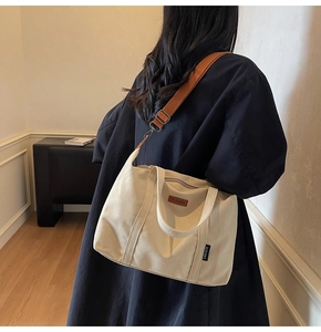 Model wearing a large cream canvas tote bag with a brown wide shoulder strap for commuting