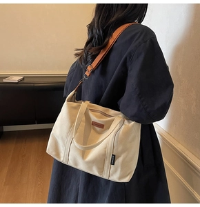 Detailed shot of beige canvas tote bag with brown leather strap worn by a model