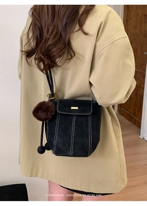 Detail of retro black bucket bag with white contrast stitching and a plush ball charm