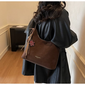 Detail of a brown suede tote bag with a floral bear charm and printed text on the surface