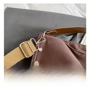 Detail of silver metal carabiner hook on brown canvas tote bag with leather strap