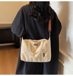 Detail of off-white canvas tote showing leather logo patch and adjustable shoulder strap