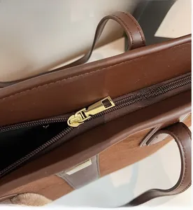 Close-up detail of smooth gold metal zipper and brown leather texture on a tote bag