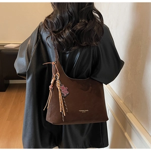 Detail of dark brown suede shoulder bag with woven fringe tassel and leopard heart charm