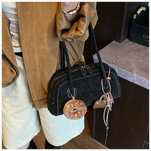 Detail of black suede shoulder bag with white contrast stitching and plush donut charms