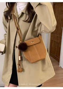 Detail of caramel bucket bag with contrast stitching and fuzzy pom pom charm