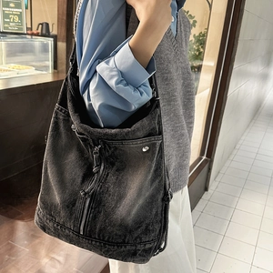 Detailed close-up of washed denim crossbody bag featuring metal rivets and zipper details