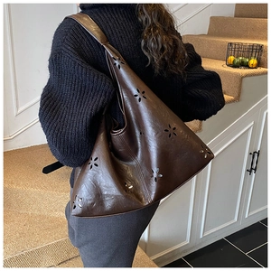 Détail macro du sac hobo marron foncé avec motifs floraux ajourés au laser