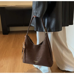Brown leather hobo bag with tassel detail and adjustable strap on a female model