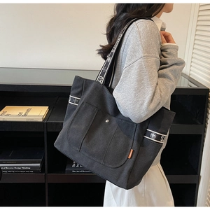 Detail view of large black canvas tote bag showing contrasting straps and button pocket