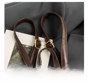 Détail des bretelles réglables en similicuir marron et boucles dorées sur un sac à dos à carreaux