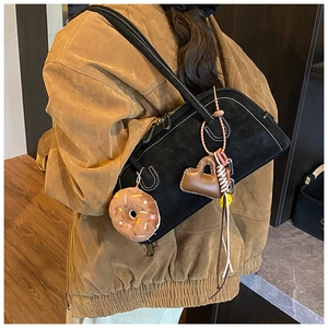 Detail of black suede shoulder bag with white contrast stitching and donut charm accessories