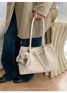 Detail of minimalist cream faux leather tote bag with long handles and plush bunny charm