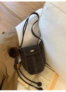 Detail of retro bucket bag featuring white contrast stitching and a plush pompom charm