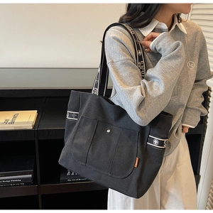 Detail view of black canvas tote bag with front pocket and branded lettered webbing straps