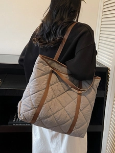 Quilted gray tote bag with brown leather straps shown on a model in a modern interior
