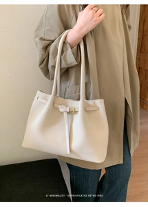 Detail of cream white tote bag with thin leather strap and metal buckle on trench coat
