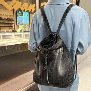 Back view of a washed denim backpack showing vertical zipper pocket and shoulder straps
