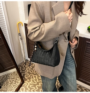 Close-up of a black woven leather hobo bag worn by a model in a smart casual outfit