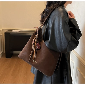 Detail of dark brown leather tote with tassel charm and retro shoulder bag texture