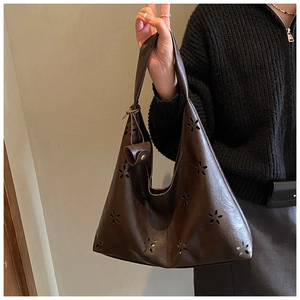 Détail du motif floral ajouré sur le sac fourre-tout marron porté par un mannequin