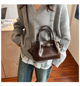 Detail of dark brown leather handbag with buckle strap and beaded charm accessory