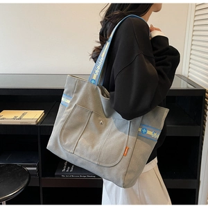 Detail of grey-green canvas tote bag with woven shoulder strap and metal snap button