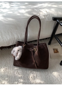Gros plan du sac cabas en daim marron avec boucle dorée et breloque en peluche
