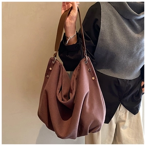 Detail of a large brown canvas tote bag with smooth leather handles and metal hardware