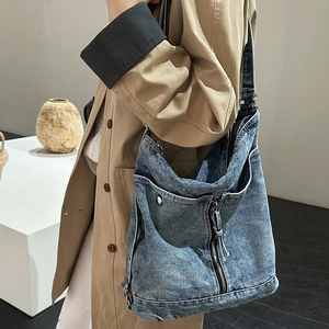 Detail of blue washed denim crossbody bag featuring vintage textures and silver zippers