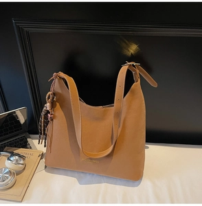 Detail view of brown faux leather tote bag with fringe charm and laptop on office desk